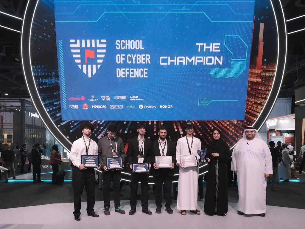 The champion team holding their awards on the GISEC stage under the School of Cyber Defense screen